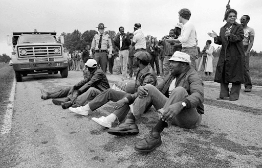 Protestors sitting in the road blocking the delivery of toxic waste to a landfill in their community. 